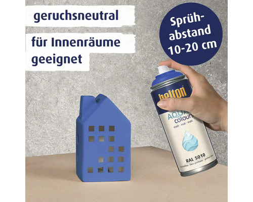Eine Hand verwendet eine Sprühdose Belton Aqua Colours matt RAL 5010, um ein kleines Hausmodell zu besprühen, geeignet für Innenräume.