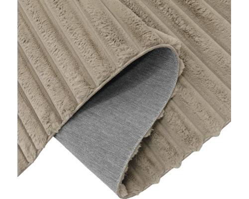 Ein Teppich mit weicher Struktur und geripptem Design, dessen Ecke umgeschlagen ist und die Rückseite zeigt.