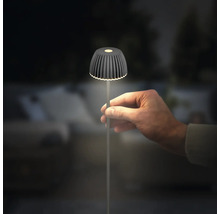 Eine Hand hält eine kleine, moderne LED Tischleuchte mit geripptem Schirm und schlankem Ständer in einer dunklen Umgebung.