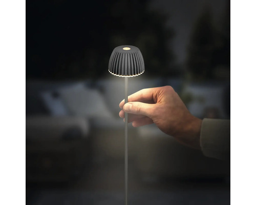 Eine Hand hält eine kleine, moderne LED Tischleuchte mit geripptem Schirm und schlankem Ständer in einer dunklen Umgebung.