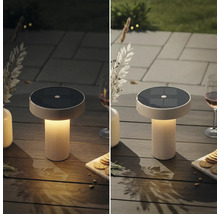Eine runde Solar Tischleuchte mit geriffeltem Standfuß steht auf einem Holztisch im Außenbereich bei Tag und Dämmerung.