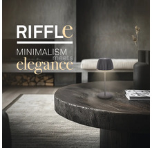 Moderne Tischleuchte im minimalistischen Design auf einem runden Holztisch in einem elegant eingerichteten Wohnzimmer.