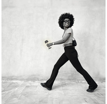 Eine Frau mit Afro-Frisur geht und hält eine kleine, tragbare Tischleuchte in der Hand.