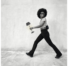Eine Frau mit Afro frisur trägt eine moderne Tischleuchte als Accessoire wie eine Handtasche.