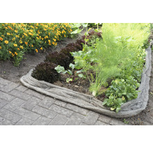 Bordure de jardin en laine de mouton servant de barrière naturelle pour un potager avec des légumes et des fleurs sur un sol pavé.