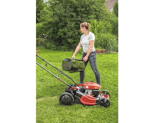 Une femme vide le bac de ramassage d''une tondeuse à gazon sur une pelouse.
