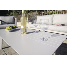 Gartenszene mit Couch, Tisch, Weinflasche und Gläsern für entspannte Stunden im Freien.