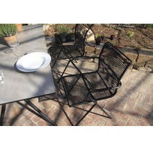 Scène avec deux chaises en cordage noires et une table à manger à l''extérieur