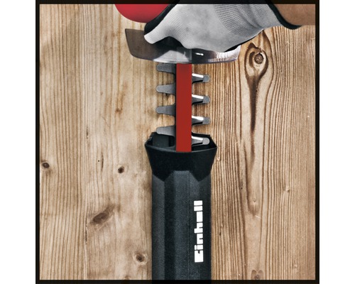Taille-haie Einhell en utilisation avec gant devant un mur en bois