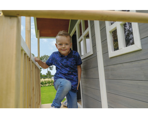 Ein Junge steht auf der Veranda eines Holzspielhauses mit Fenstern.