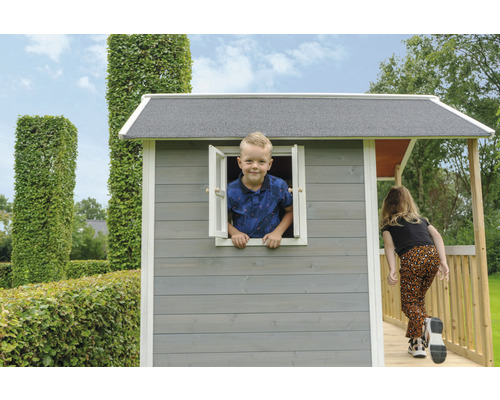 Cabane de jeu avec enfant à la fenêtre et fille sur la véranda dans le jardin