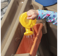 Un enfant verse de l''eau avec un arrosoir jaune dans une table de jeu