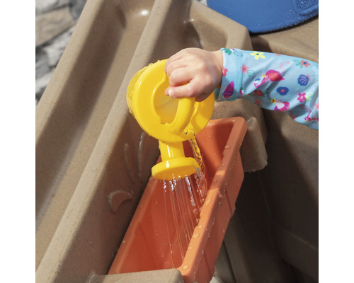 Un enfant verse de l''eau avec un arrosoir jaune dans une table de jeu