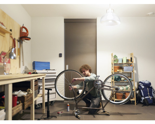 Un homme répare un vélo dans un atelier avec un établi et une étagère