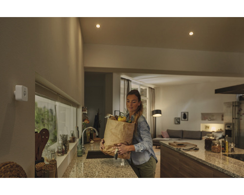 Femme avec un sac de courses dans la cuisine sous des plafonniers et un détecteur de mouvement.