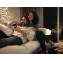 Paar entspannt auf einem Sofa in einem hellen Wohnzimmer, Mann schaut auf sein Smartphone