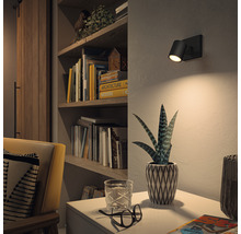 Wohnzimmer mit Bücherregal, Sessel und einer schwarzen Wandleuchte