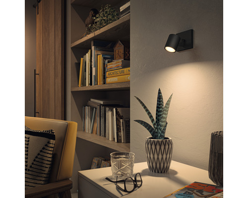 Wohnzimmer mit Bücherregal, Sessel und einer schwarzen Wandleuchte