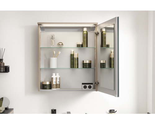 Armoire de toilette ouverte avec étagères en verre et divers articles de salle de bains.