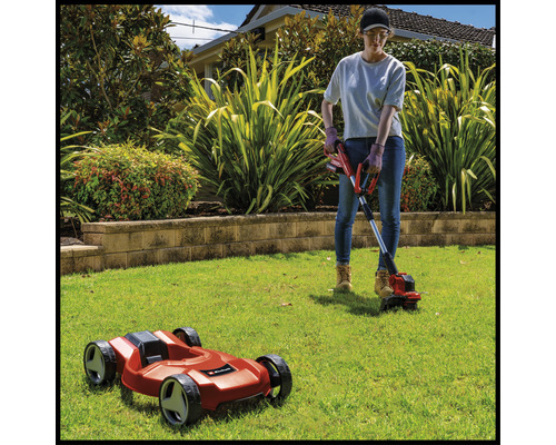 Une femme travaille dans le jardin avec un coupe-bordure et un robot tondeuse.