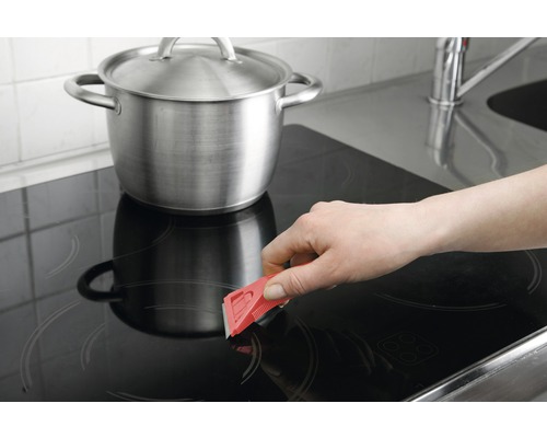 Nettoyage d''une plaque de cuisson avec un grattoir à côté d''une casserole