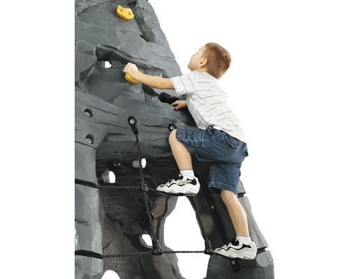 Un enfant grimpe sur un mur d''escalade gris avec des prises jaunes et un filet de corde noir.