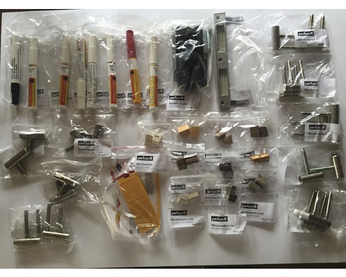 Assortiment de matériaux de réparation, comprenant des stylos de retouche, des ferrures et de la cire molle dans des emballages en plastique.