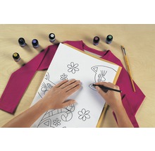 Szene mit einer Person, die ein Katzenmuster mit einem Stift auf ein Blatt Papier zeichnet, zusammen mit Textilfarbe, einem Pinsel und einem T-Shirt.