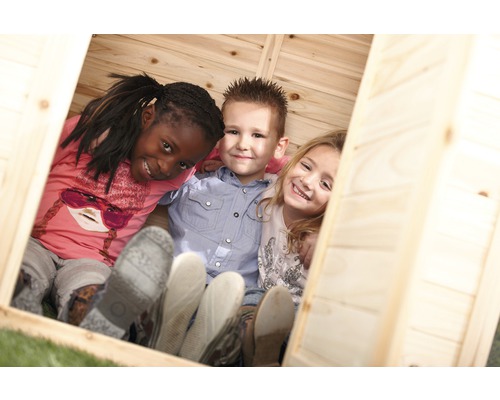 Drei Kinder lachen in einem Spielhaus aus Holz in die Kamera.