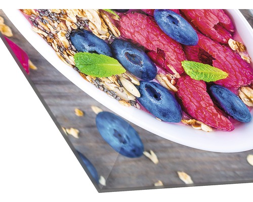 Nahaufnahme einer Schale mit Müsli, Himbeeren, Heidelbeeren und Minze auf einem Holztisch