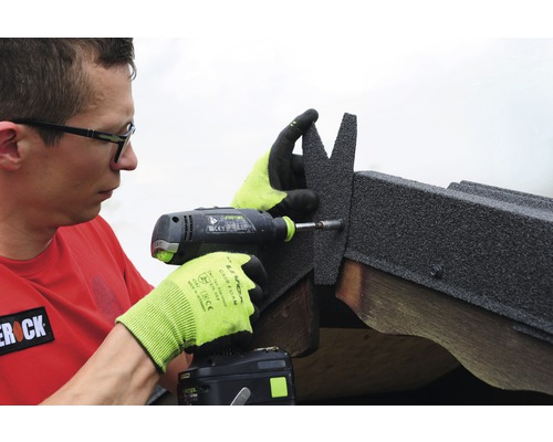 Un homme fixe des bardeaux de toiture avec une visseuse sans fil