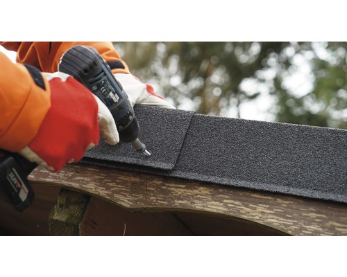 Une personne fixe un bardeau bitumé avec une visseuse sans fil