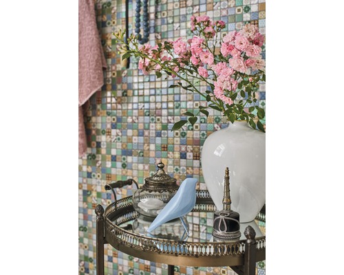 Arrangement décoratif avec fleurs, oiseau, théière et flacon sur une table d''appoint devant un mur en mosaïque