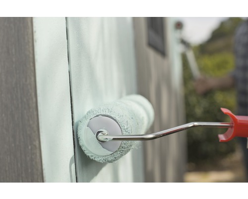 Nahaufnahme einer Person, die eine Holzwand mit einer Farbwalze streicht