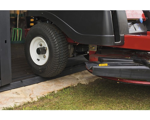 Aufsitzrasenmäher fährt über eine Gummischwelle in ein Gartenhaus