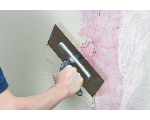 Un artisan lisse du mastic avec une spatule sur un mur.