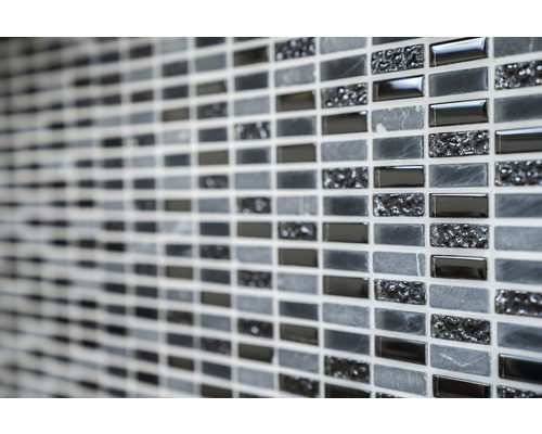 Detailaufnahme einer Wand mit Mosaikfliesen in verschiedenen Grautönen und Texturen.