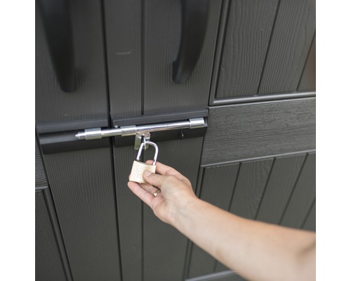 Une personne ferme un abri de jardin avec un cadenas.