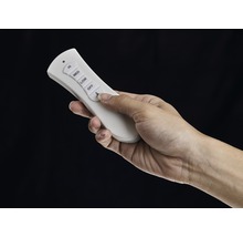 Eine Hand bedient eine weiße Fernbedienung für einen Deckenventilator.