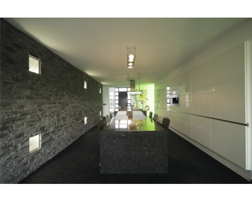 Pièce lumineuse avec mur décoratif en pierre, table à manger et kitchenette.