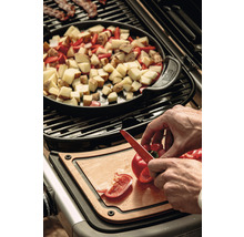 Zubereitung von Speisen auf einem Grill mit Kartoffeln, Paprika und Speck, wobei eine Person Paprika auf einem Schneidebrett schneidet.