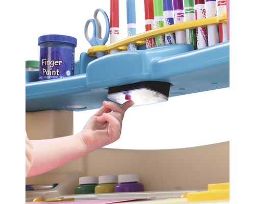 Vue détaillée d''une table d''enfant avec des peintures au doigt, des feutres et une lampe intégrée, manipulée par un enfant.