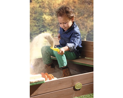 Un enfant joue avec un moule jaune dans un bac à sable avec banc.