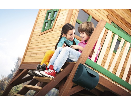 Zwei Kinder sitzen auf der Treppe eines Holzspielhauses und telefonieren mit einem Spielzeugtelefon.