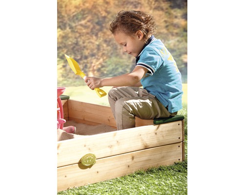 Garçon jouant avec une pelle jaune dans un bac à sable en bois.
