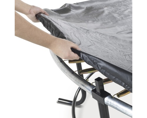 Une personne place une bâche de protection de trampoline sur un trampoline