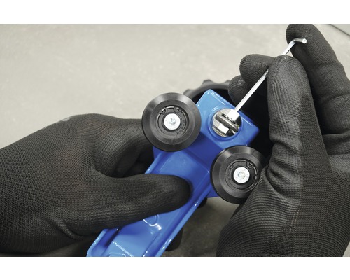 Gros plan sur des mains gantées ajustant une carrelette bleue avec une clé Allen.