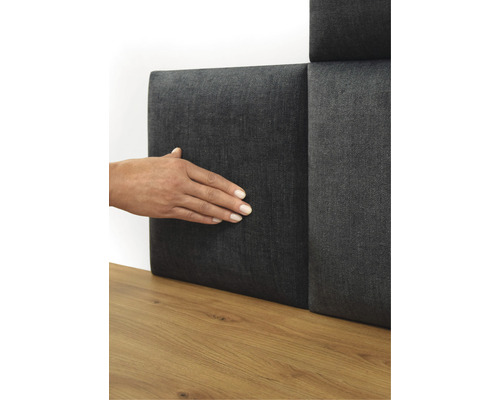 Person berührt graues Wandpaneel mit Textilbezug auf einem Holzboden.