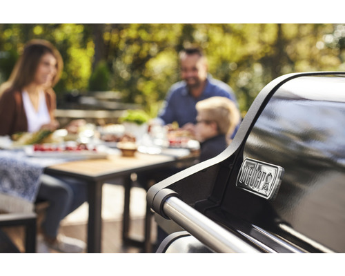 Familie grillt im Garten mit einem Weber Grill. Weber Logo.