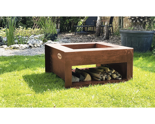 Quadratische Feuerschale aus Stahl mit Holzscheiten auf einer Wiese